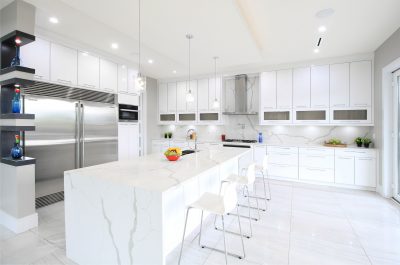 Notice how elegantly you can feature special items in the custom crafted corner piece seen at far left of this modern white kitchen that has matching quartz back splash and large island.